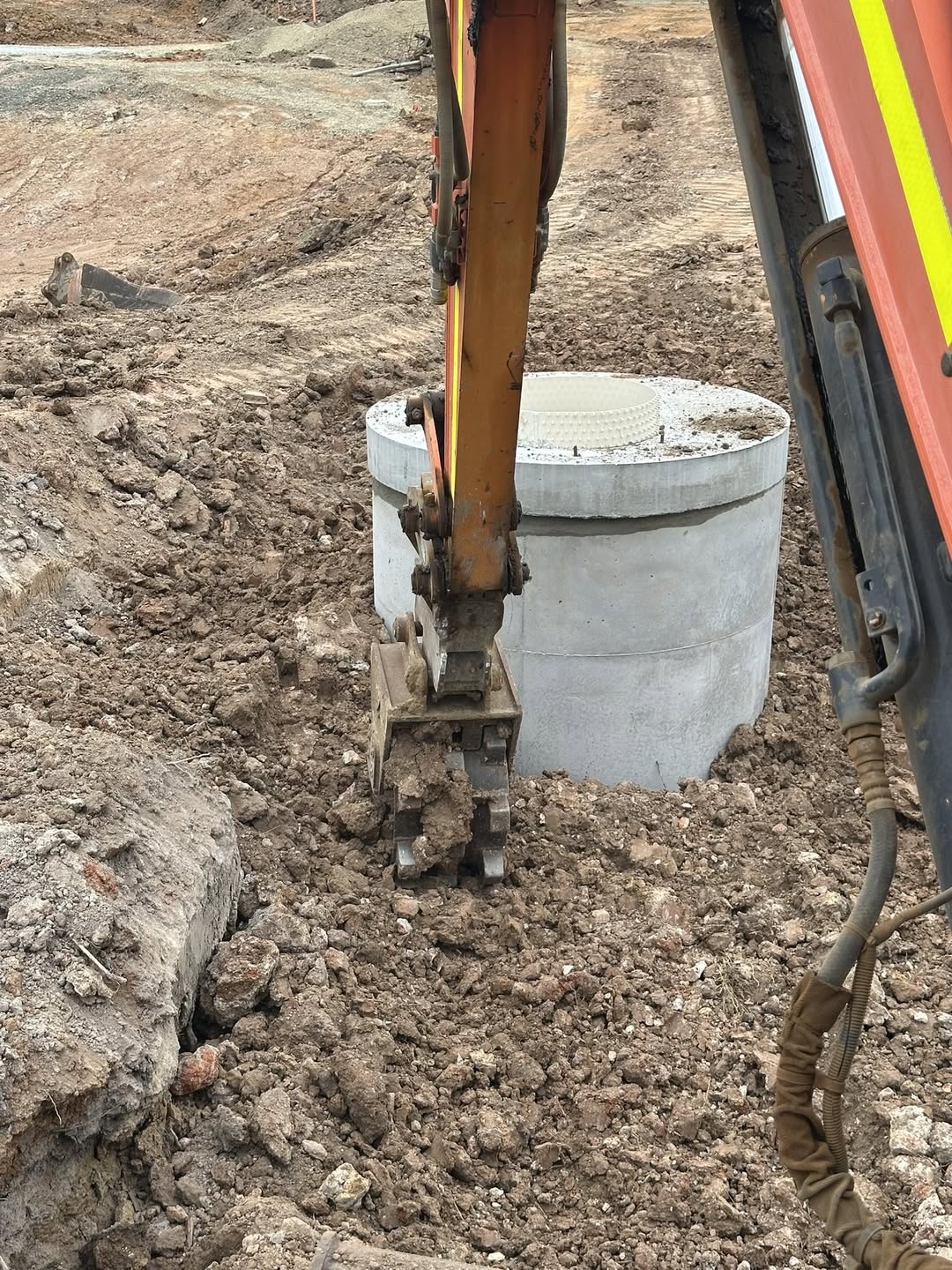 Excavator working beside a concrete drainage pit