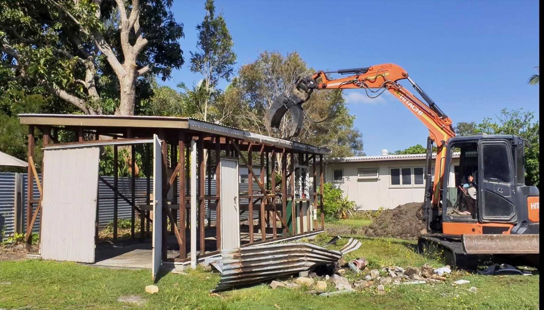 Excavator dismantling a backyard shed