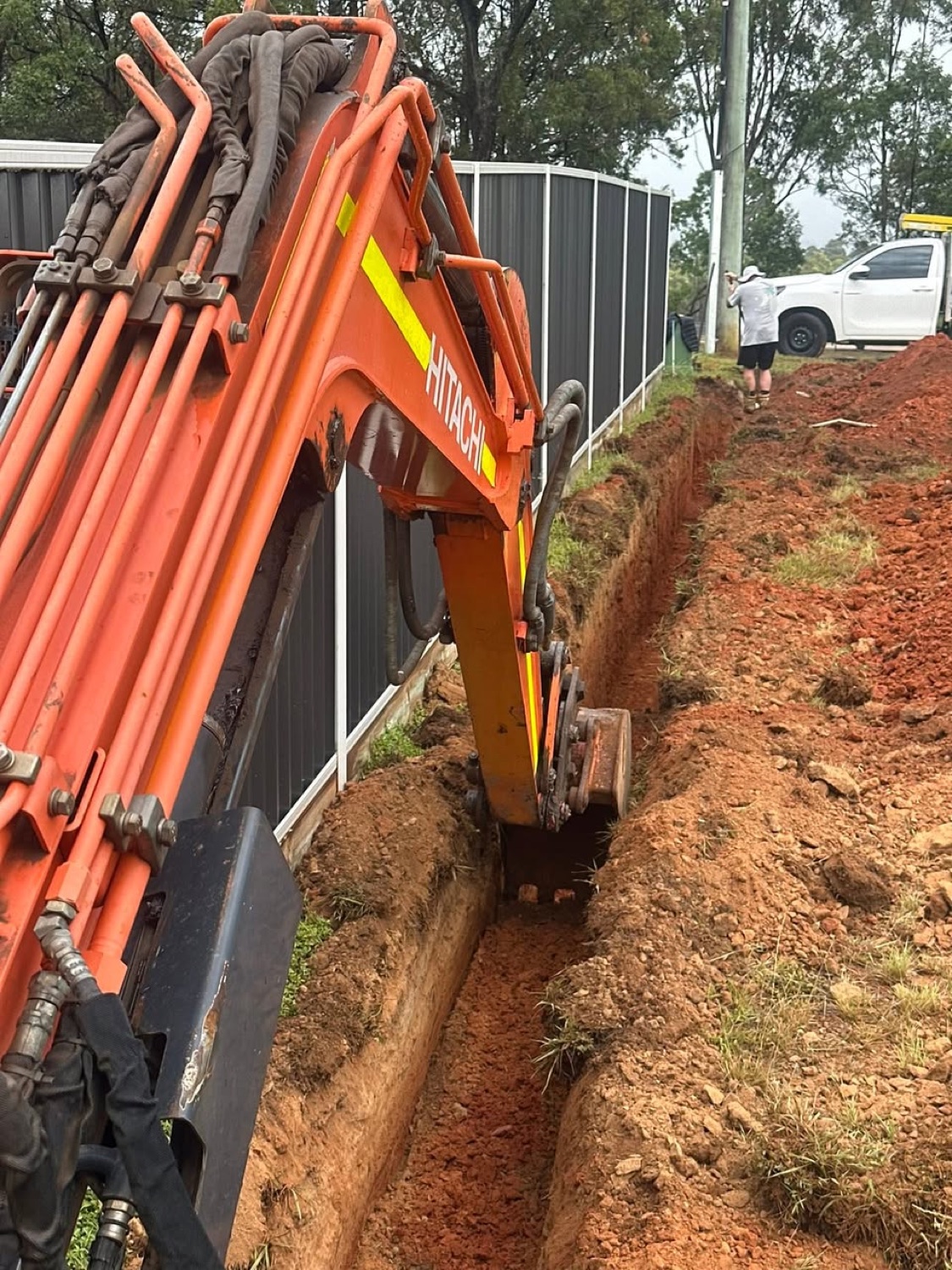 Excavator trenching beside a boundary fence